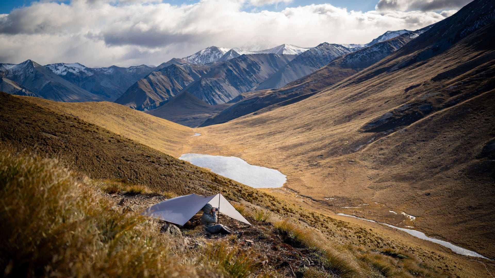 Mountain landscape with a small shelter and lake, under a cloudy sky.