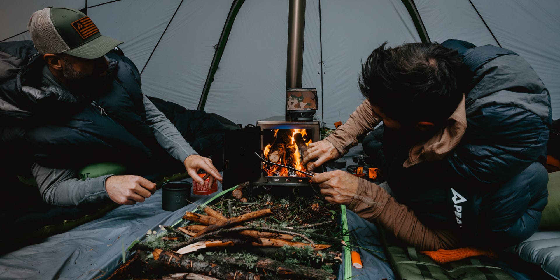 Two hunters, inside their Solace Sleeping Bags feeding the fire.