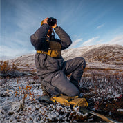 Hunter on a sit pad in the STATIC down jacket and pant, glassing a snowy basin