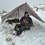 Hunter sitting in snow under a tarp, wearing down hunting pants