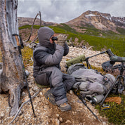 Hooded hunter in the jacket and pant glassing from a rocky saddle